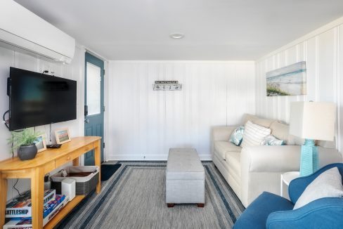 A bright, coastal-themed living room with a mounted tv, beige furniture, and nautical accents.