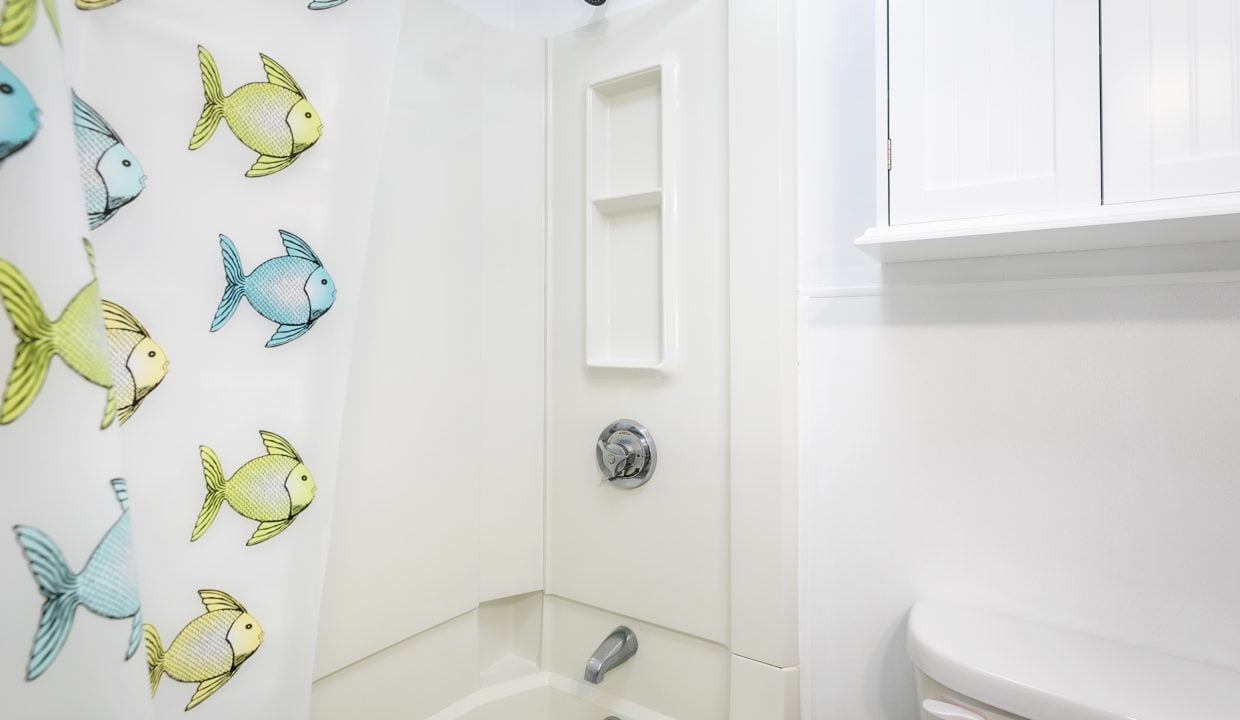 A clean, white bathroom corner with a shower featuring a curtain with fish patterns.