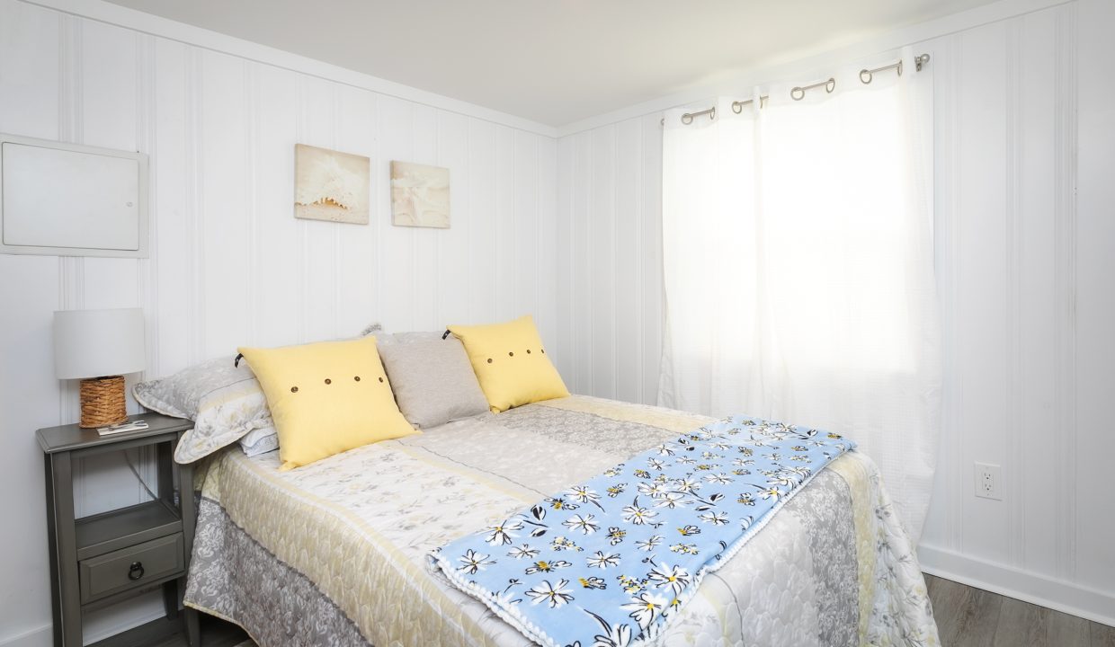 Bright and cozy bedroom with a double bed, patterned bedding, yellow accent pillows, and wall art with a seaside theme.