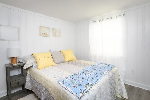 Bright and cozy bedroom with a double bed, patterned bedding, yellow accent pillows, and wall art with a seaside theme.