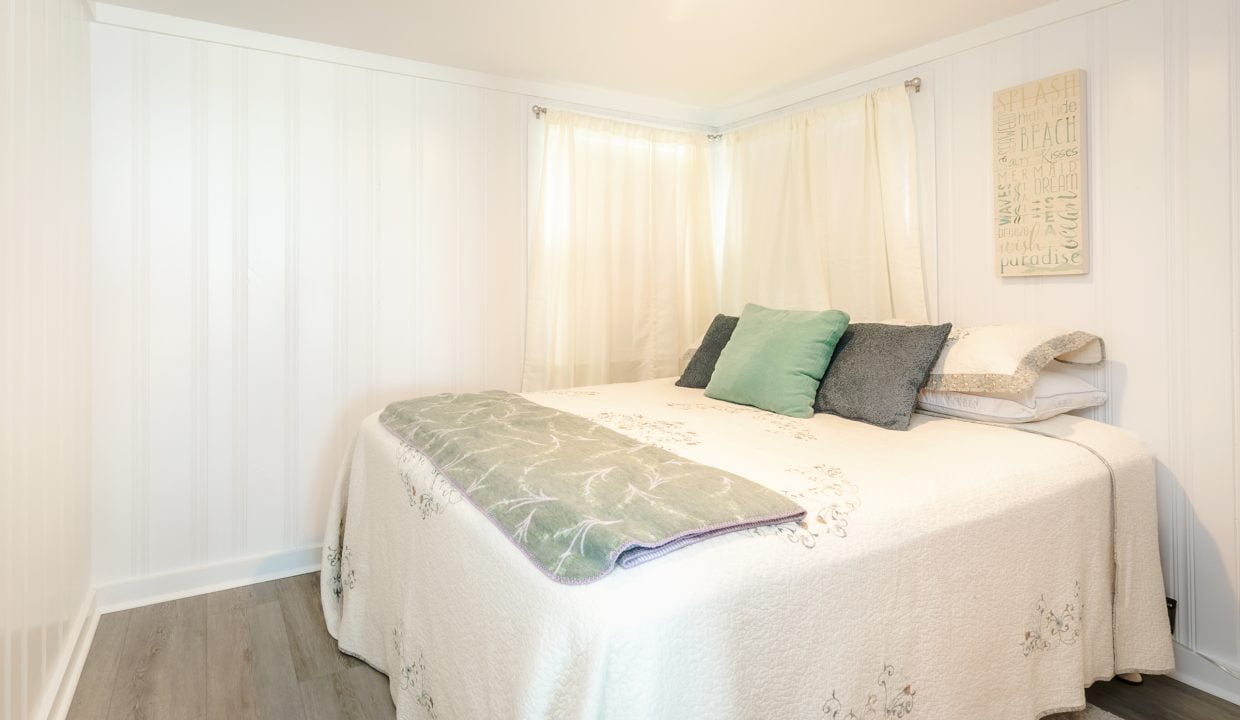 Brightly lit bedroom with a neatly made bed, white walls, and decorative pillows.