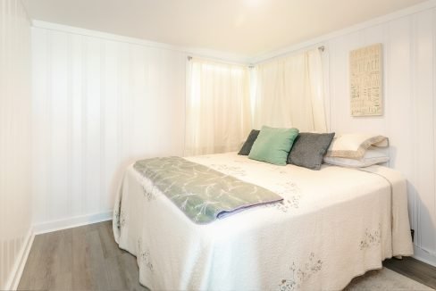 Brightly lit bedroom with a neatly made bed, white walls, and decorative pillows.