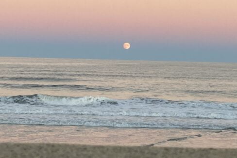 a full moon is seen over the ocean.