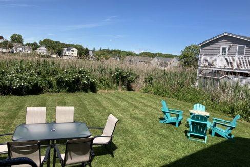 a lawn with a table and chairs and a house in the background.