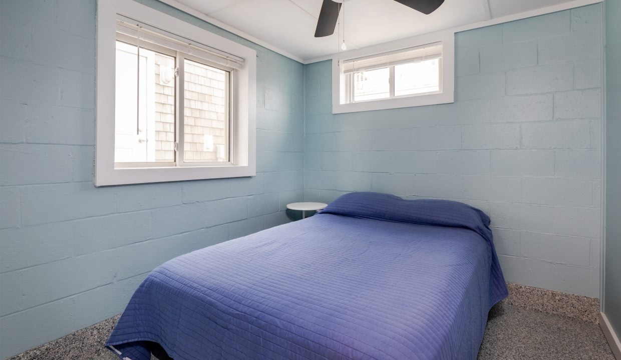 a blue bed in a small room with a ceiling fan.