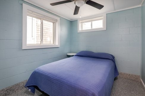 a blue bed in a small room with a ceiling fan.