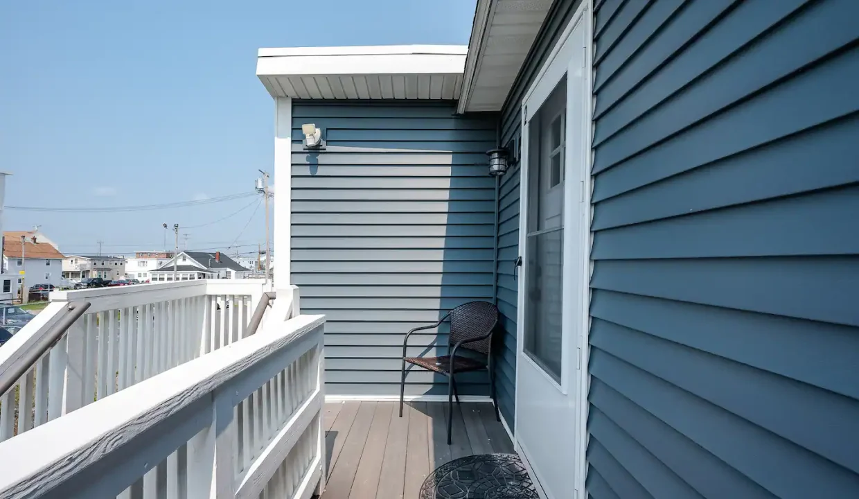 A small balcony with a single chair overlooking a coastal neighborhood.