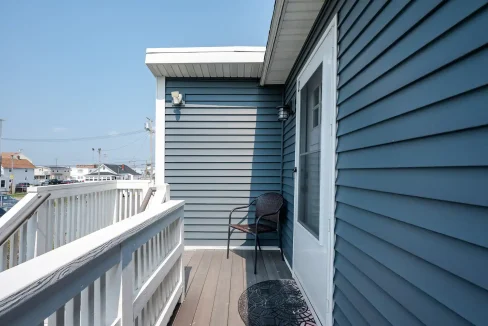 A small balcony with a single chair overlooking a coastal neighborhood.