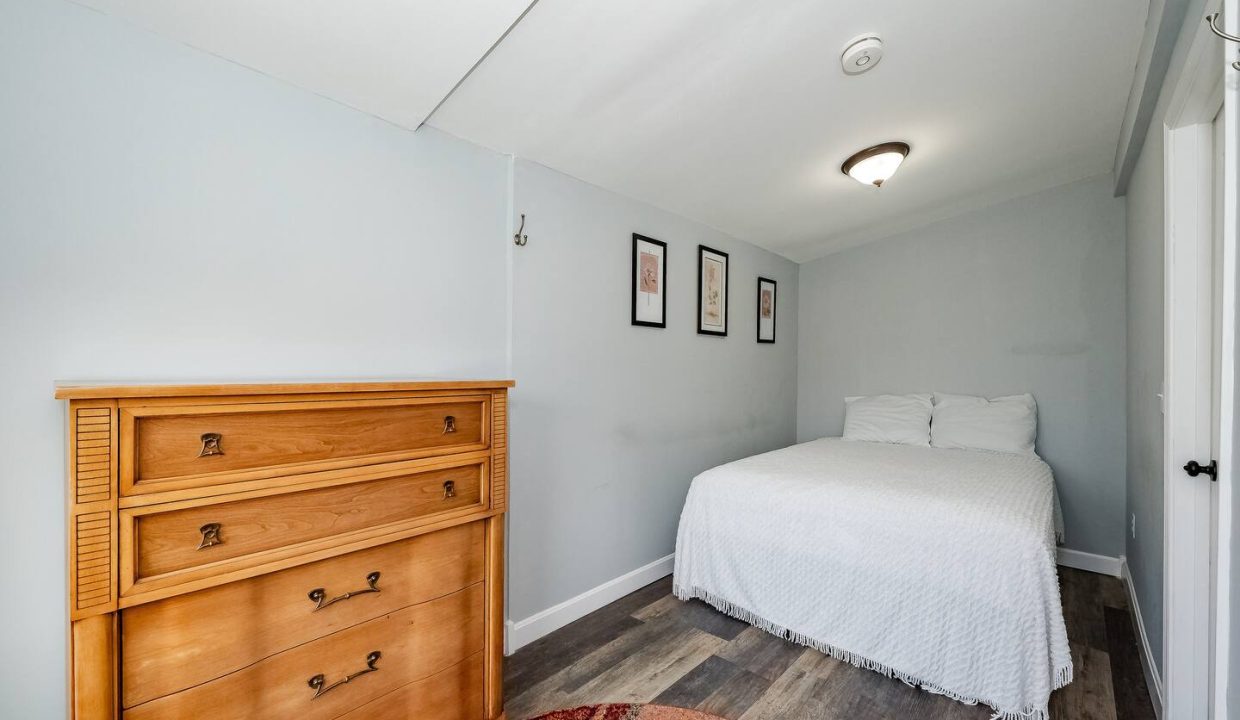 A neatly presented bedroom with a single bed, wooden dresser, and decorative rug.