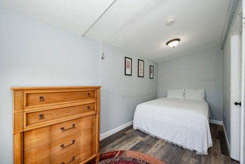 A neatly presented bedroom with a single bed, wooden dresser, and decorative rug.