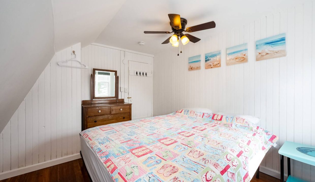 Cozy attic bedroom with slanted ceilings, a ceiling fan, and beach-themed decor.