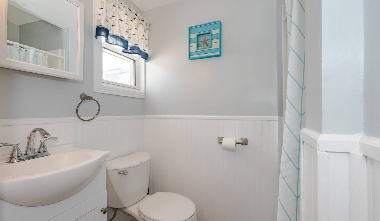 A clean and bright bathroom with white walls, featuring a pedestal sink, toilet, and nautical-themed decor.