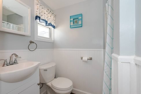 A clean and bright bathroom with white walls, featuring a pedestal sink, toilet, and nautical-themed decor.
