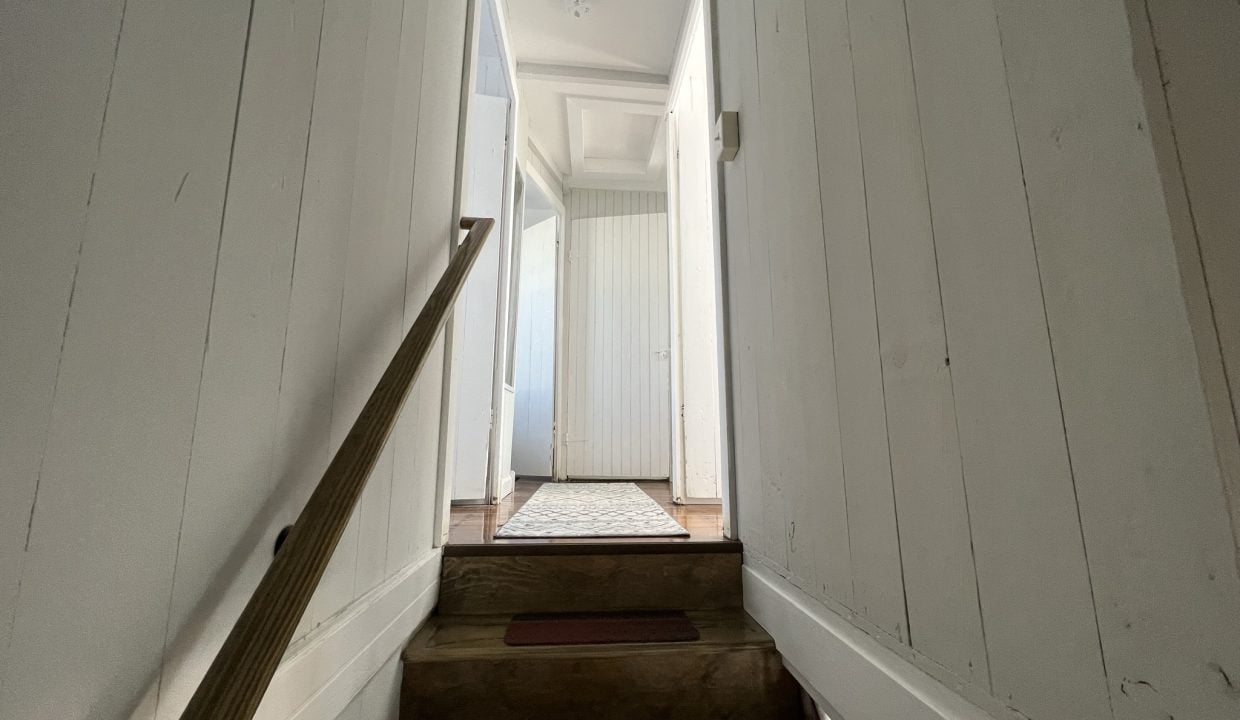 a long narrow hallway with a door and a light fixture.