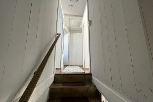 a long narrow hallway with a door and a light fixture.