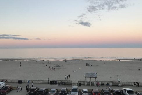 A view of the beach at dusk with cars parked in the parking lot.