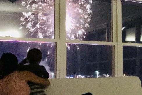 A woman and a child watching fireworks from a window.