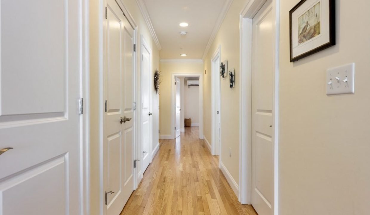 a long hallway with white doors and wood floors.