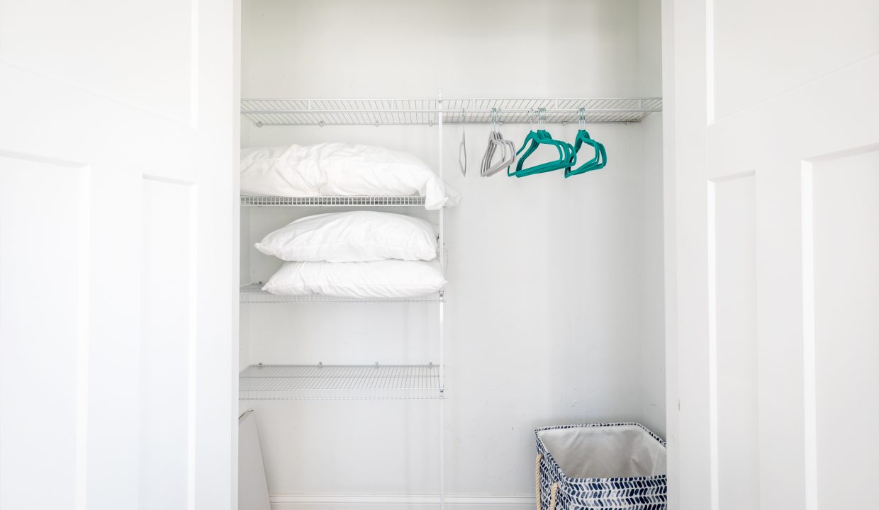 a white closet with clothes and a basket.