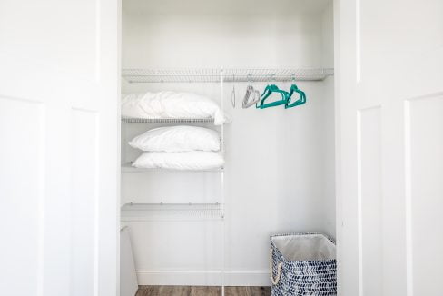 a white closet with clothes and a basket.