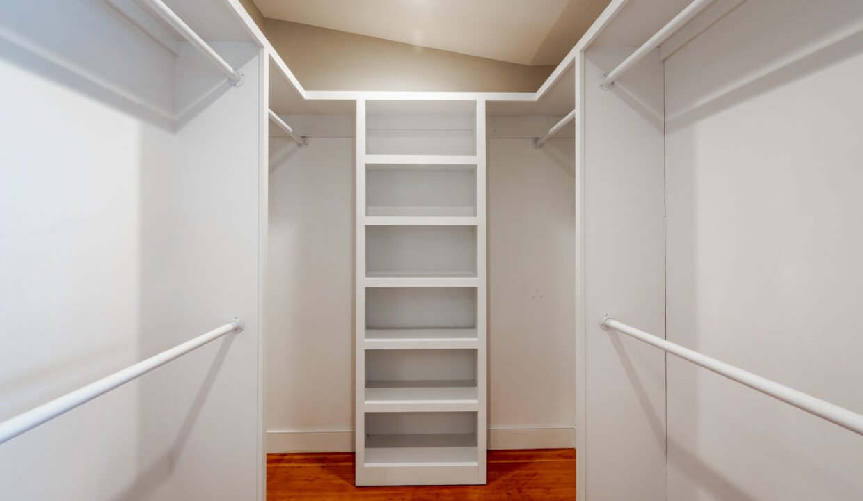 a walk in closet with white shelving and wood flooring.