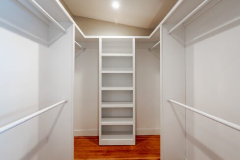 a walk in closet with white shelving and wood flooring.
