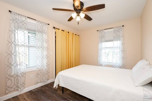 Bright and minimalistic bedroom with a large bed, geometric pattern curtains, and a ceiling fan.