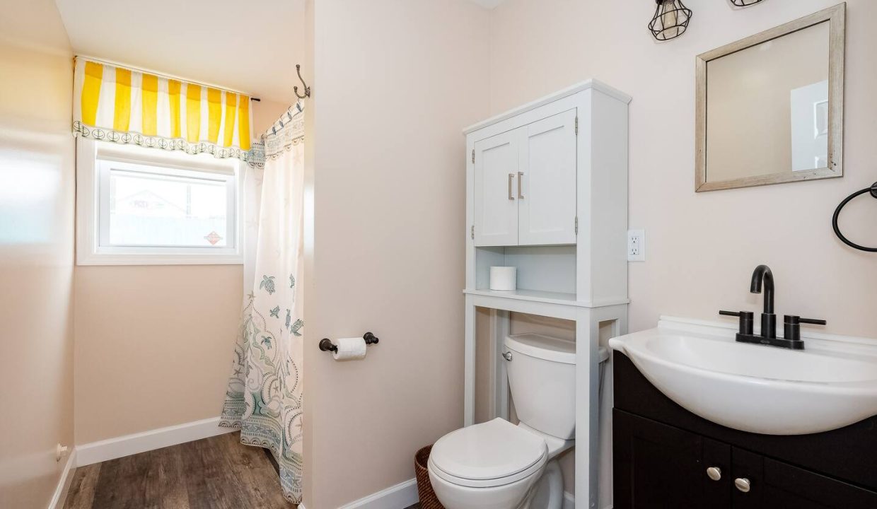 A bright, clean bathroom with white walls, a dark vanity, and a patterned shower curtain.