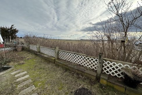 a wooden fence in a grassy area next to a field.