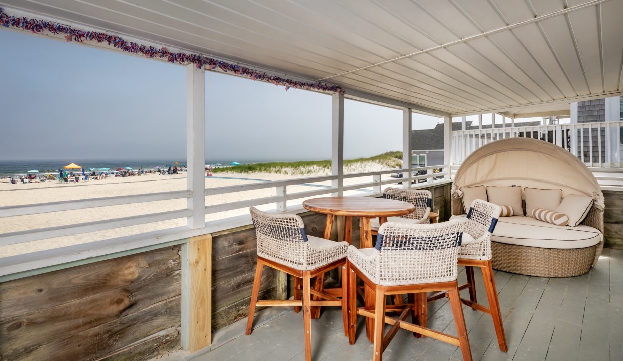 a porch with a table and chairs overlooking the beach.