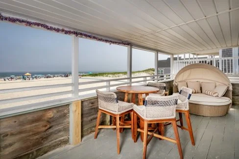 a porch with a table and chairs overlooking the beach.
