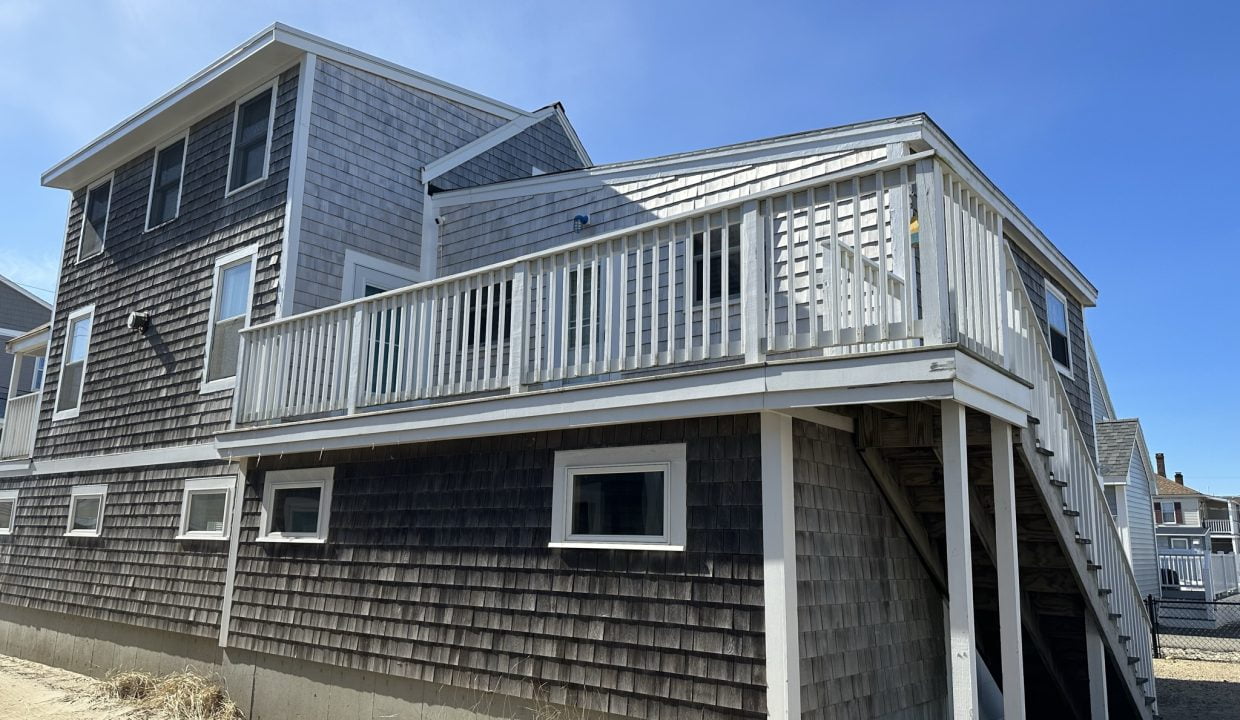 a beach house with a deck and stairs leading to the second floor.
