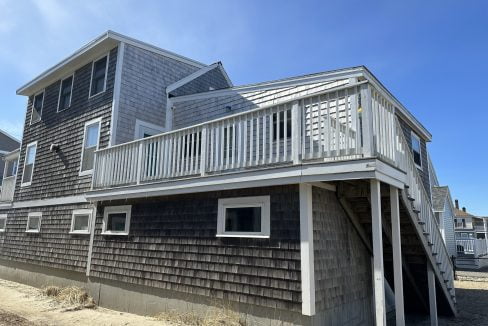 a beach house with a deck and stairs leading to the second floor.