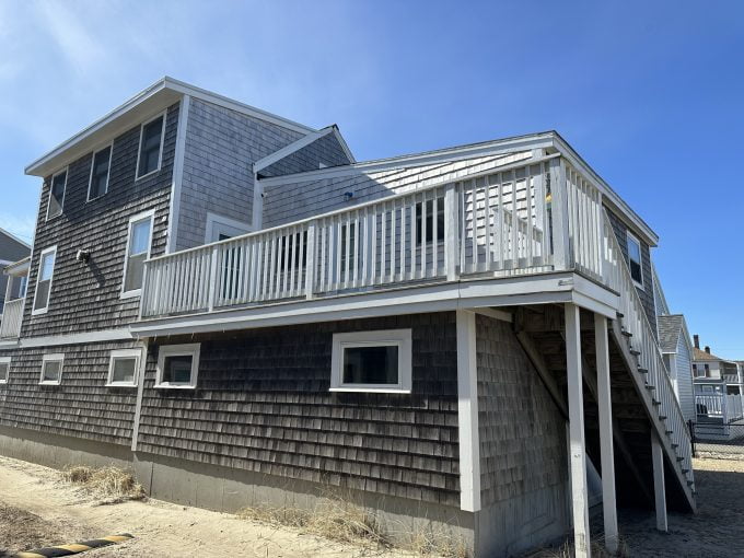 a beach house with a deck and stairs leading to the second floor.