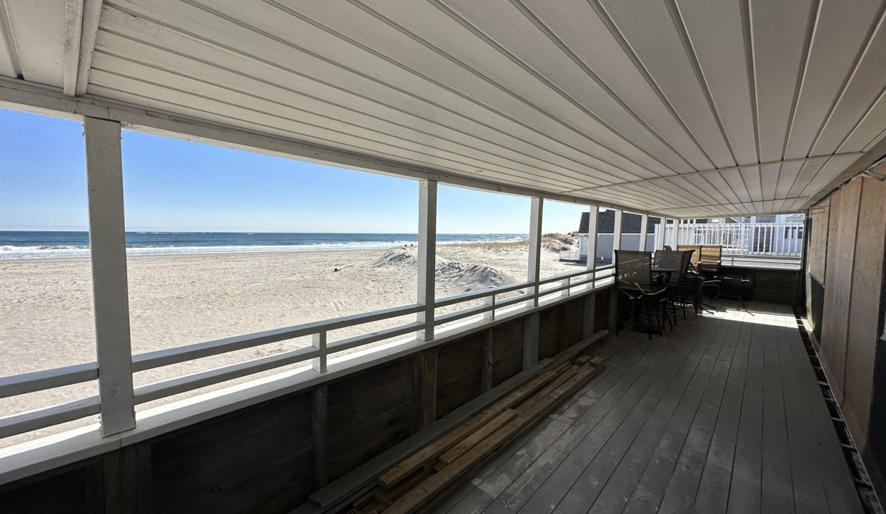 a covered porch with a bench and a view of the beach.