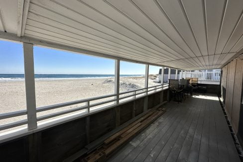 a covered porch with a bench and a view of the beach.