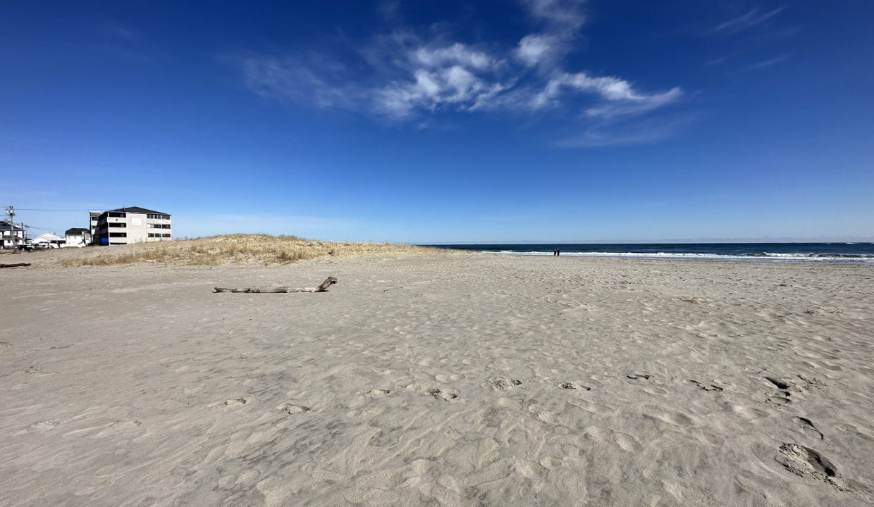 a sandy beach with a house in the distance.