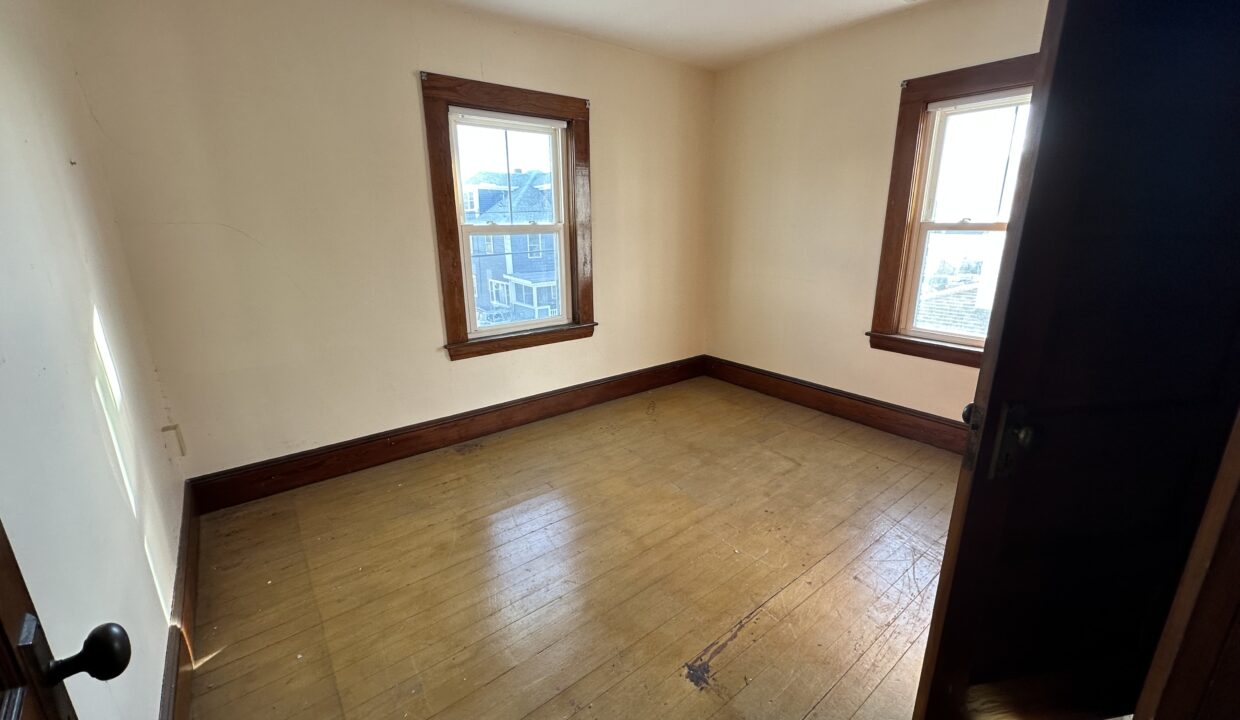 an empty room with two windows and a hard wood floor.