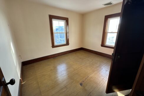 an empty room with two windows and a hard wood floor.