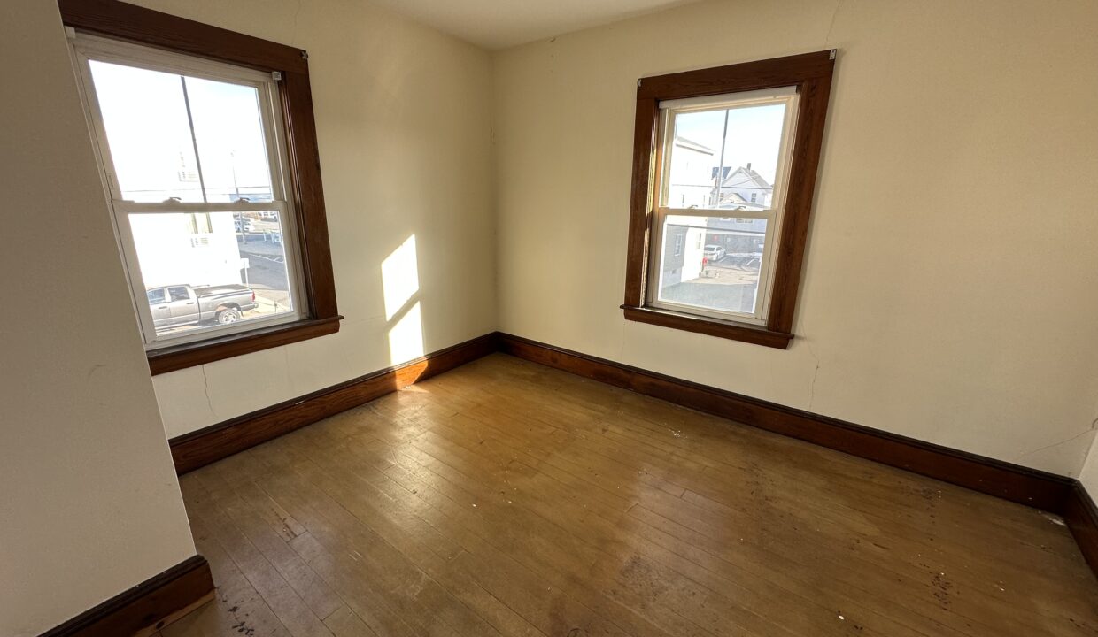 an empty room with two windows and a hard wood floor.