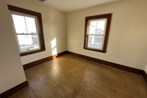 an empty room with two windows and a hard wood floor.