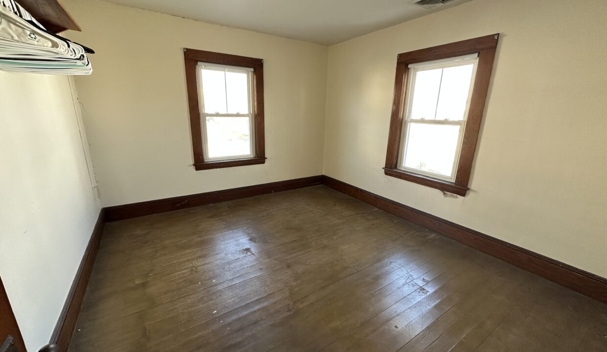 an empty room with two windows and a hard wood floor.