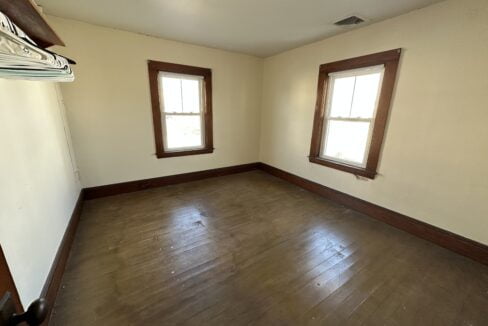 an empty room with two windows and a hard wood floor.