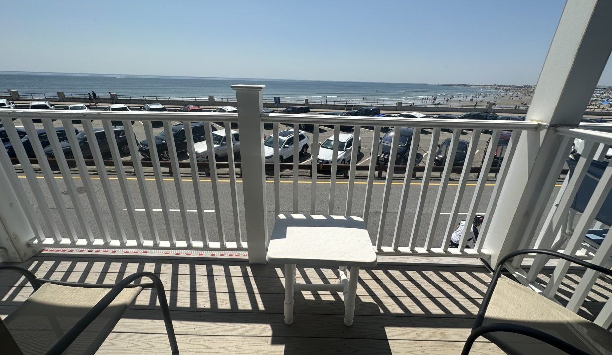 a chair and table on a deck with a parking lot and a beach.