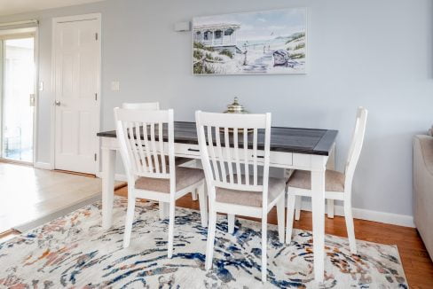 a dining room table with white chairs and a rug.