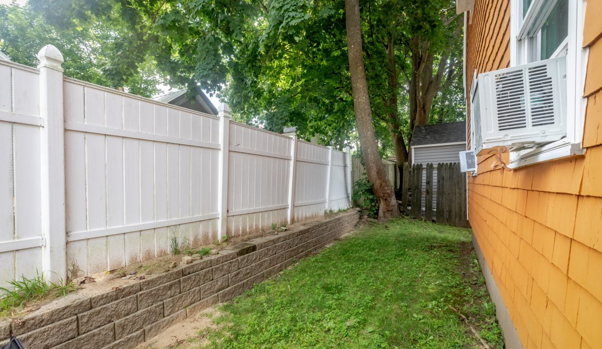 A backyard with a white fence and a tree.