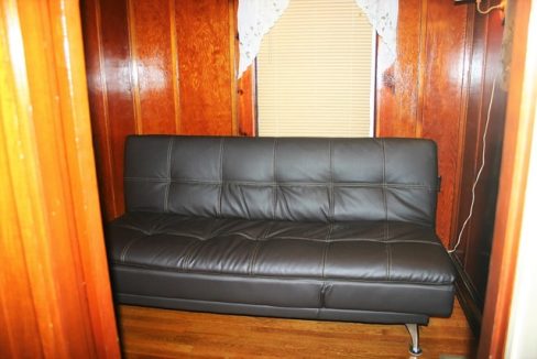 A black couch in a room with wood paneling.