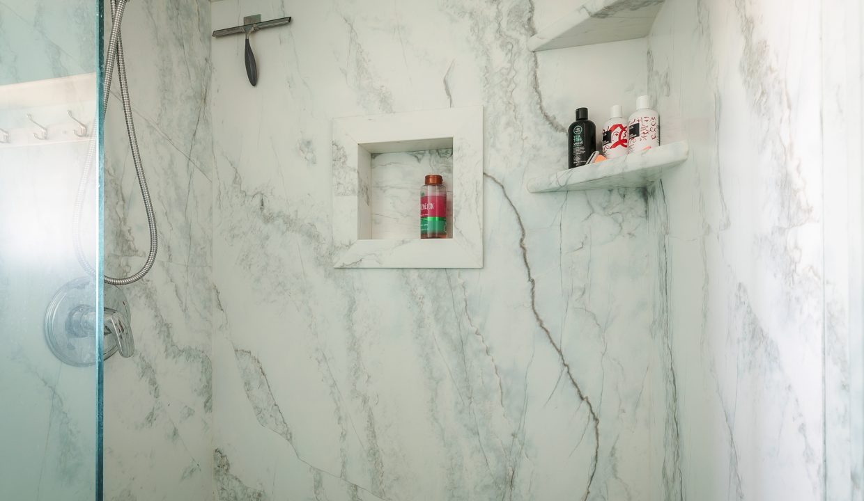 A white marble shower with blue walls and shelves.