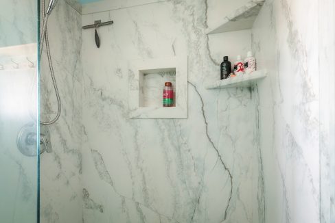 A white marble shower with blue walls and shelves.