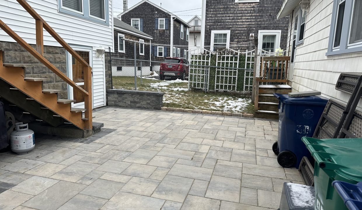 A backyard with a brick patio and a trash can.